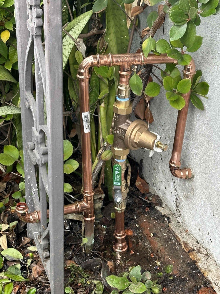 Exterior copper water lines and a pressure regulator beside a wall