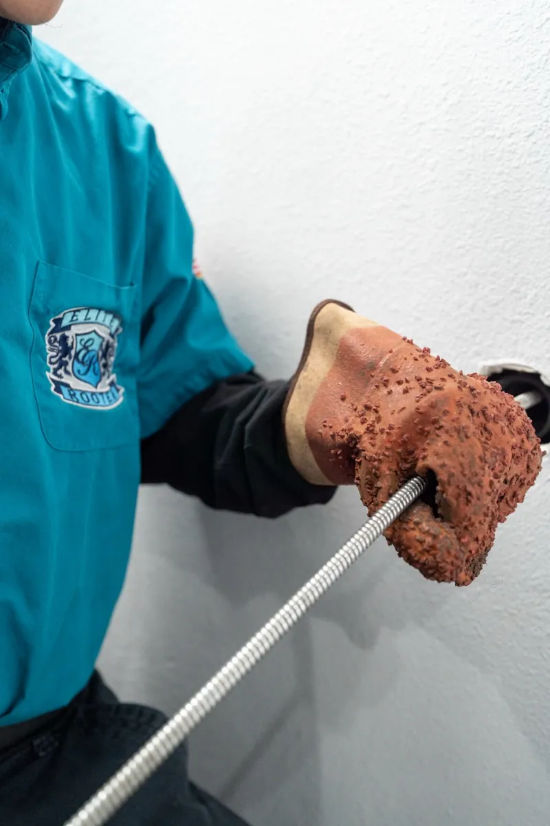 An Elite Rooter technician guiding a drain cable with gloved hands