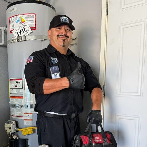 Elite Rooter technician giving a thumbs up next to a water heater while holding a plumbing tool bag.