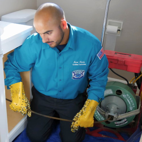 Elite Rooter technician using drain cleaning equipment in a residential bathroom while wearing protective gloves and uniform.