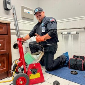 Elite Rooter technician using specialized equipment to unclog a toilet drain in a clean, tiled bathroom